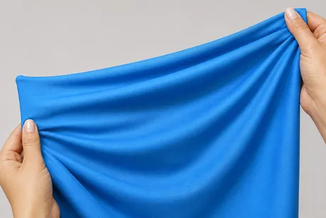 Hands stretching blue nylon spandex fabric demonstrating flexibility and proper fabric handling during garment care.