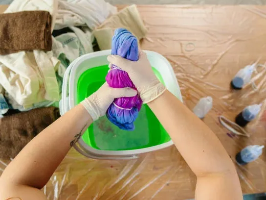 Hands dyeing nylon fabric in a colourful dye bath to demonstrate colour absorption and textile finishing techniques.