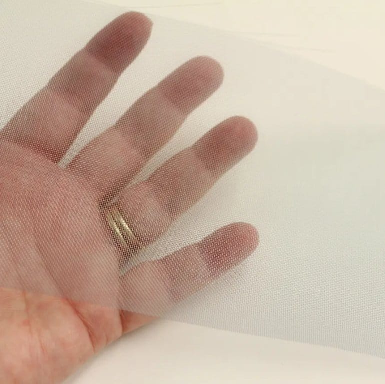 Transparent nylon mesh fabric stretched over a hand, showcasing its lightweight, breathable and flexible structure.