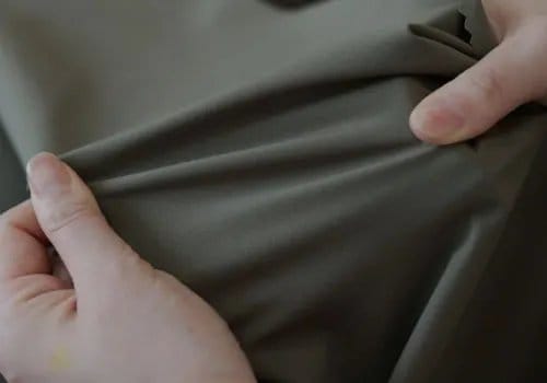 Hands stretching spandex fabric to demonstrate elasticity and recovery performance.
