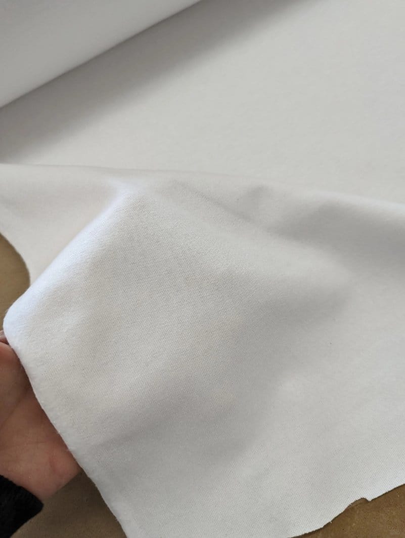 Close-up of smooth white cotton fabric held by hand, showing the fine, even surface associated with ring-spun cotton textiles.