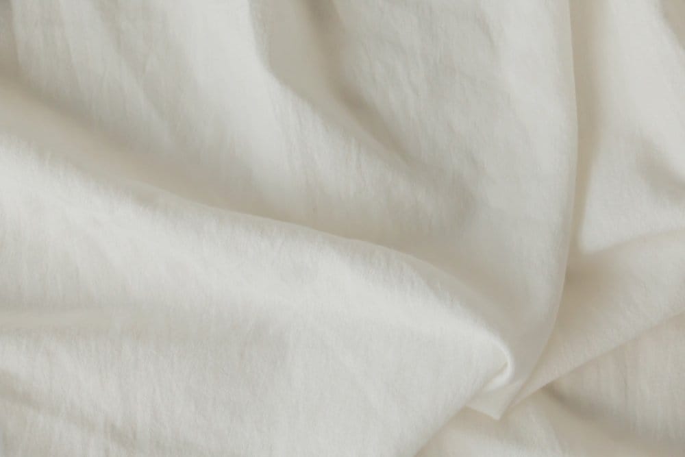 Close-up of soft white Upland cotton fabric arranged in loose folds, showing its smooth surface and lightweight texture.